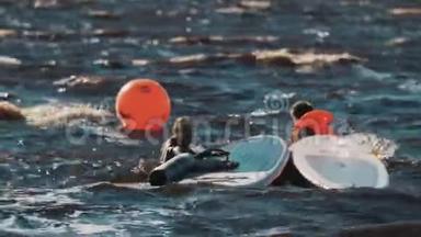 两个冲浪者漂浮在水面上，靠近冲浪板和橙色信标。 很多浪
